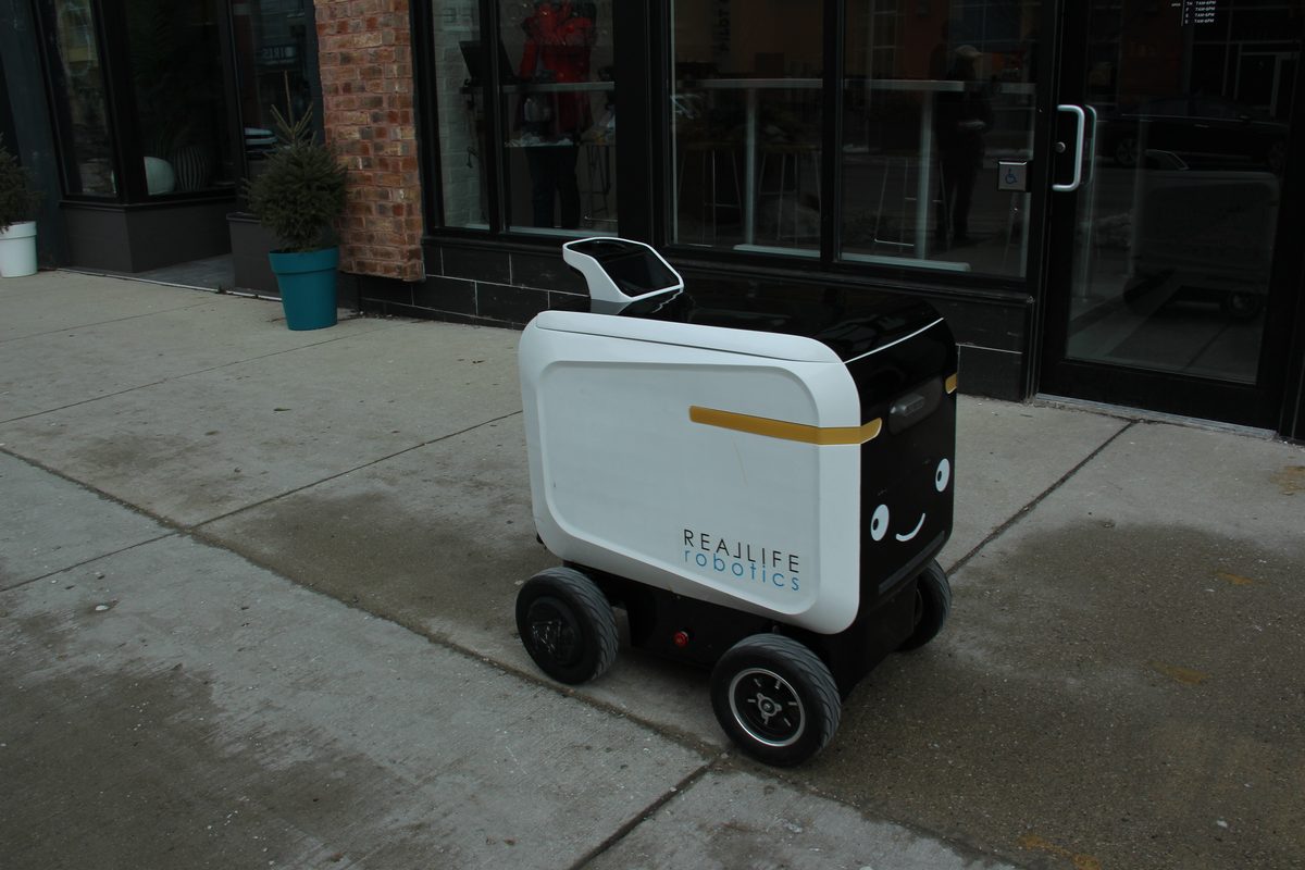 A delivery robot on a public street outside a row of shops