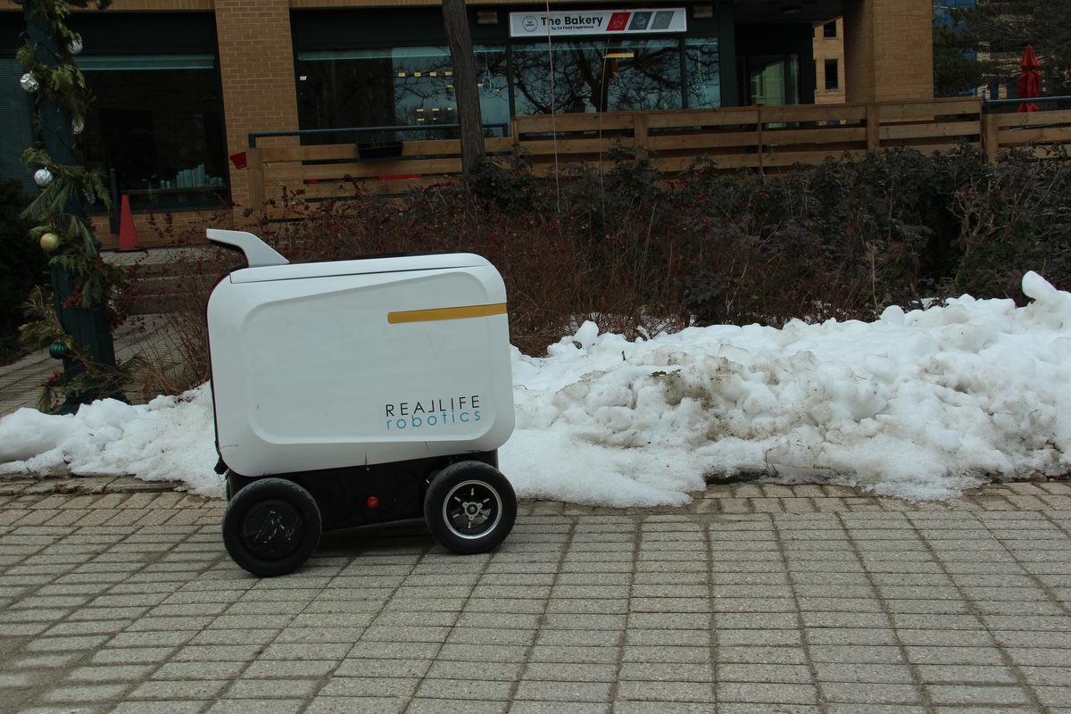 A delivery robot holding a marked path beside a snowbank