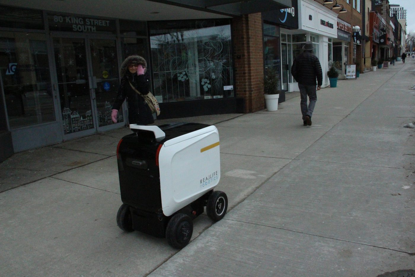 Pedestrians walk past a delivery robot on a shared city street