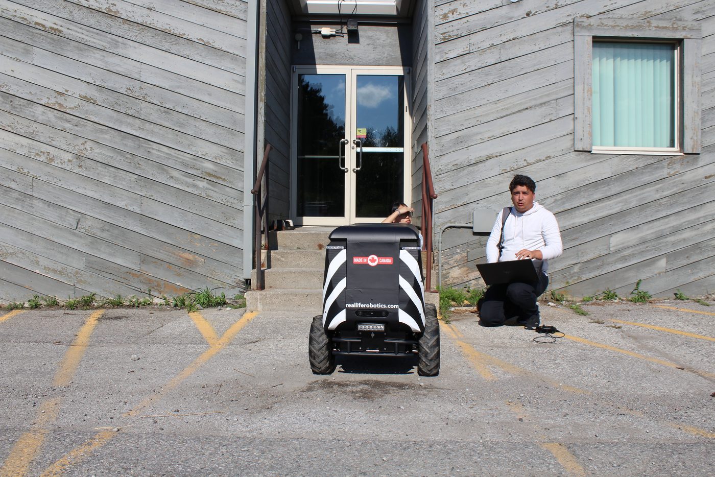 An operations technician kneels with a laptop beside a delivery robot